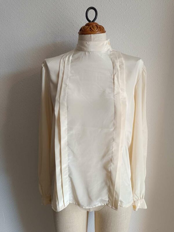 Description Chemisier vintage au style années 80, élégant et intemporel. Sa coupe fluide, son col montant discret et ses lignes verticales apportent une allure chic et soignée, idéale aussi bien pour une tenue de travail que pour un look plus rétro assumé. Fabriqué en France, ce chemisier en polyester offre une belle tenue et un tombé léger. Pièce en très bon état, soigneusement sélectionnée.