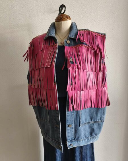 Originale veste sans manches en jean LM Lulu revisitée avec de larges franges roses et clous dorés qui lui donnent un style audacieux et très mode. Sa coupe ample permet de la porter facilement sur une robe, un top ou une chemise pour apporter une touche rock et bohème à une tenue. Une pièce forte qui attire immédiatement le regard.