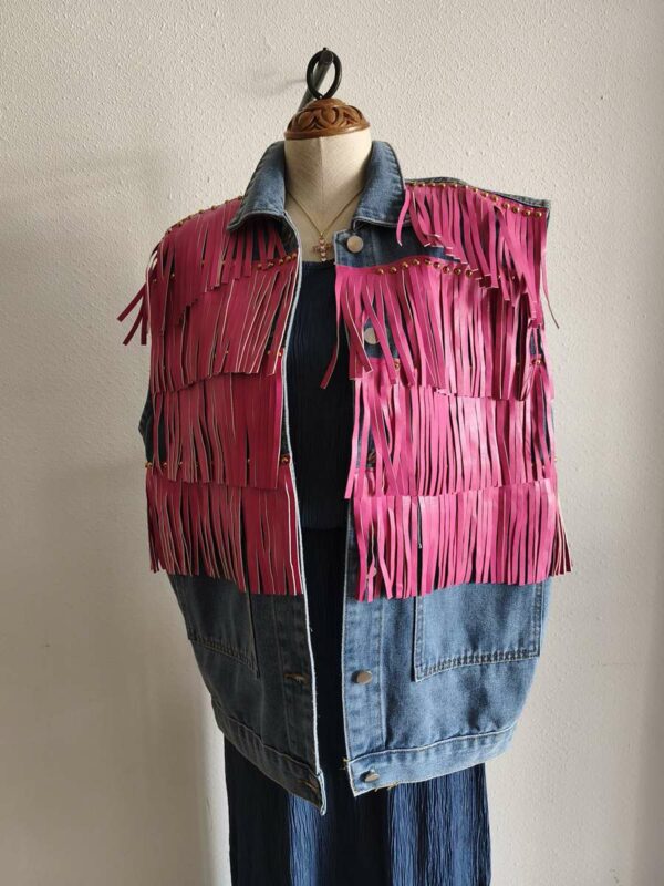 Originale veste sans manches en jean LM Lulu revisitée avec de larges franges roses et clous dorés qui lui donnent un style audacieux et très mode. Sa coupe ample permet de la porter facilement sur une robe, un top ou une chemise pour apporter une touche rock et bohème à une tenue. Une pièce forte qui attire immédiatement le regard.